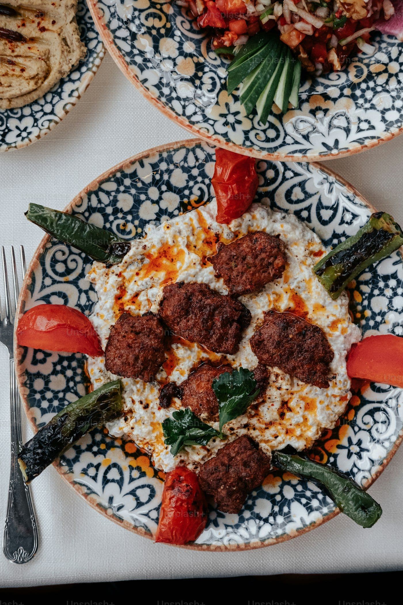 Spiced lamb kofta on a decorative plate with roasted peppers and tomatoes