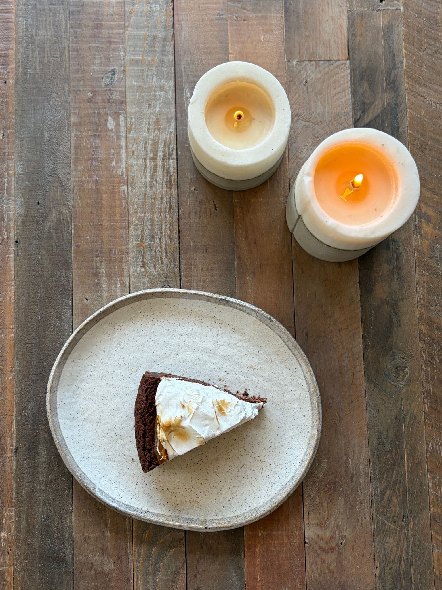 A slice of marquise on a ceramic plate, on a wooden table lit by candles