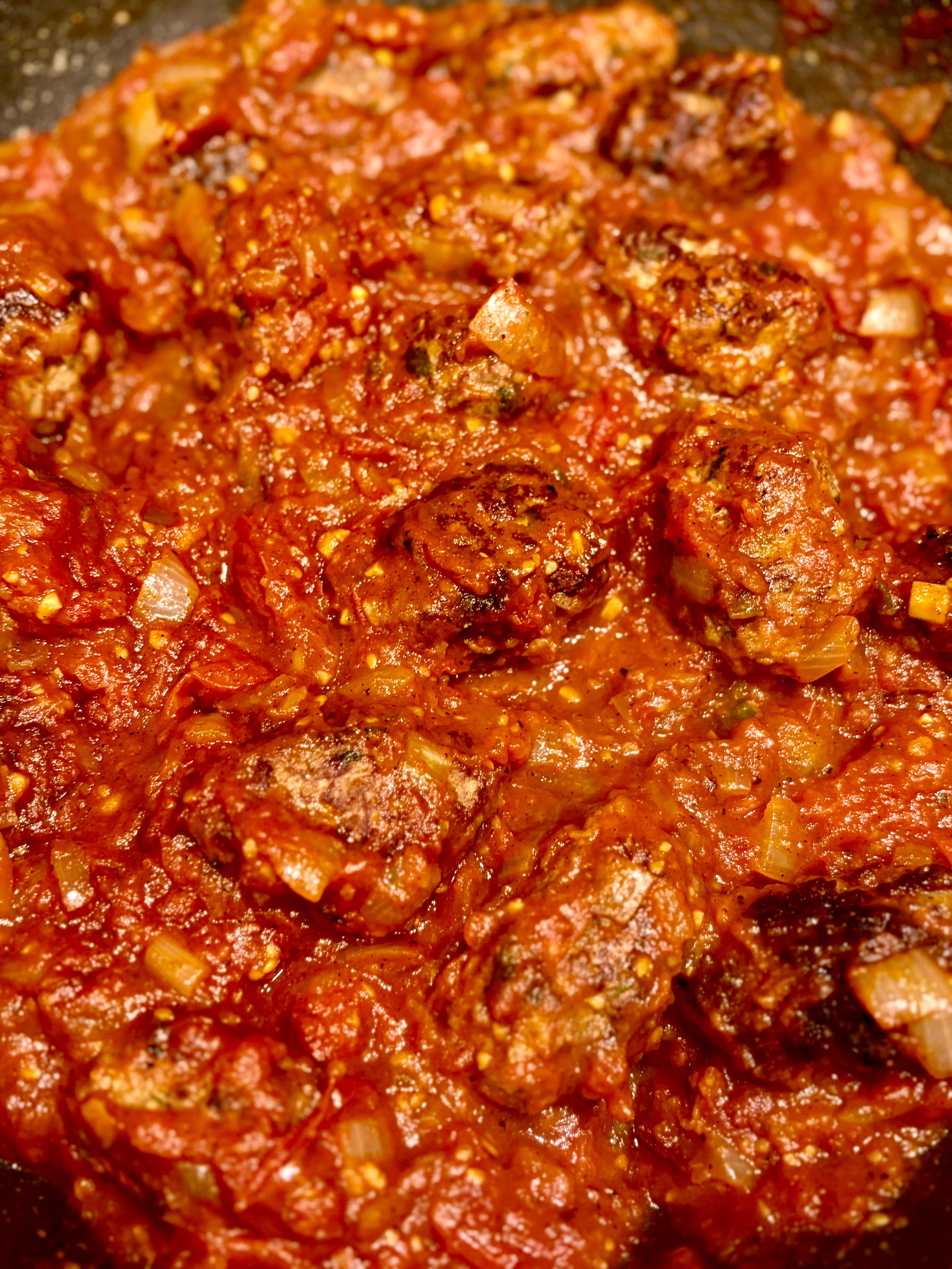 Rich harissa tomato sauce with lamb kofta cooking in the pan