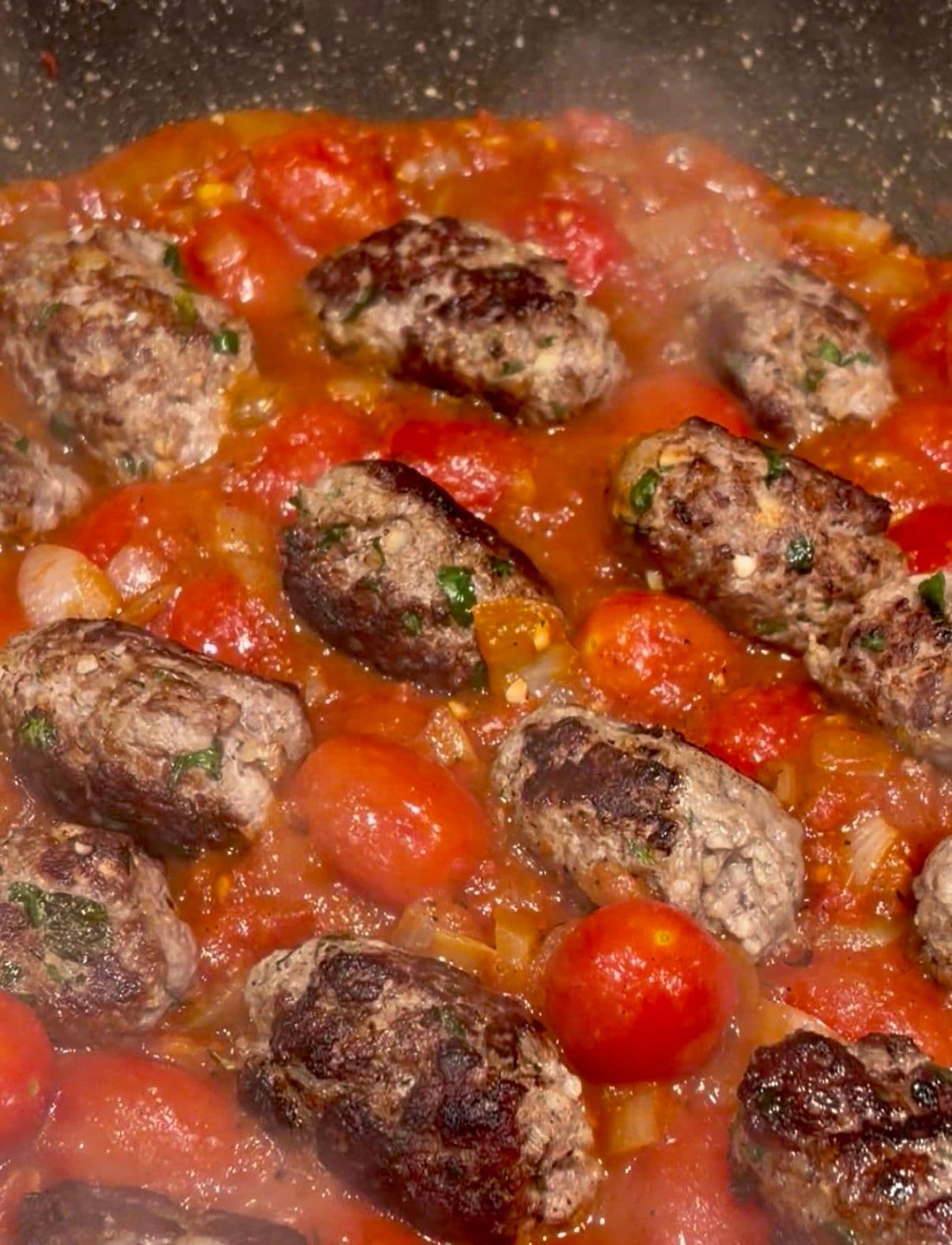 Lamb kofta simmering in harissa tomato sauce with cherry tomatoes
